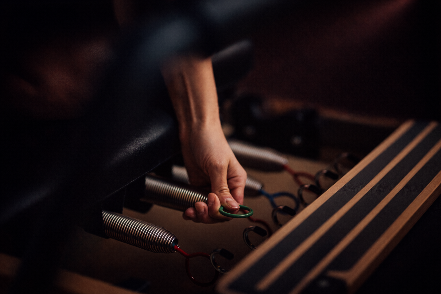 Hand of a person attaching a green ring for a Reformer Pilates